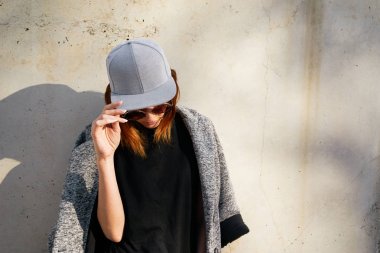 Young woman  wearing a grey blank cap and sunglasses posing against concrete wall background  clipart