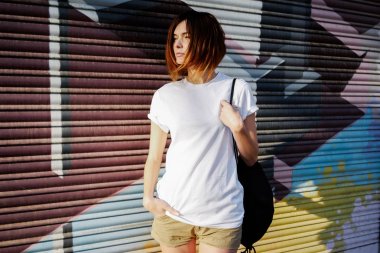bir sırt çantası bir graffiti duvar arka plan üzerinde beyaz t-shirt ayakta giyen genç çekici kadın 