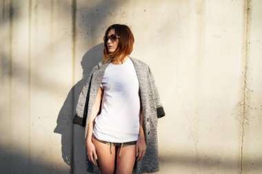 Beyaz boş t-shirt ve arka plan beton duvara karşı poz güneş gözlüğü takmış çekici genç kadın