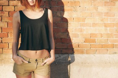 bir tuğla duvar arka planı poz kolları olmadan bir siyah boş T-shirt giyen genç kadın 