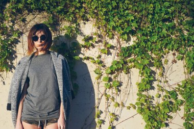 Ivy ile beton duvara bir arka plan üzerinde poz omuzları üzerinde bir gri boş t-shirt ve ceket giyen genç çekici kadın