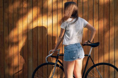 Ahşap arka plan üzerinde bisiklet ile ayakta beyaz boş t-shirt ve jeans giymiş genç sportif kadın şort