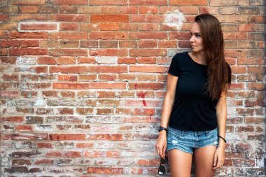 Açık duran tuğla duvar arka planı siyah boş t-shirt ve kot şort giyen uzun siyah saçlı bir genç güzel hipster kadın portresi