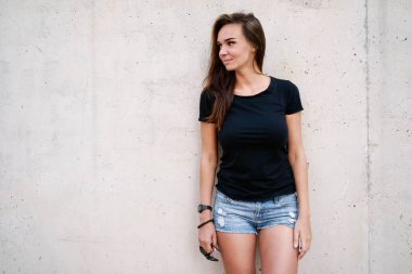 Bir boş siyah t-shirt gri beton duvar arka planı poz giyen güzel genç kadın