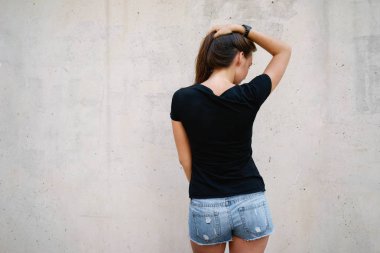 Bir boş siyah t-shirt gri beton duvar arka planı poz giyen güzel genç kadın