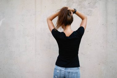 Bir boş siyah t-shirt gri beton duvar arka planı poz giyen güzel genç kadın