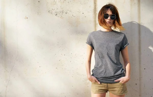 beautiful young woman wearing gray blank t-shirt posing against a background of a concrete wall