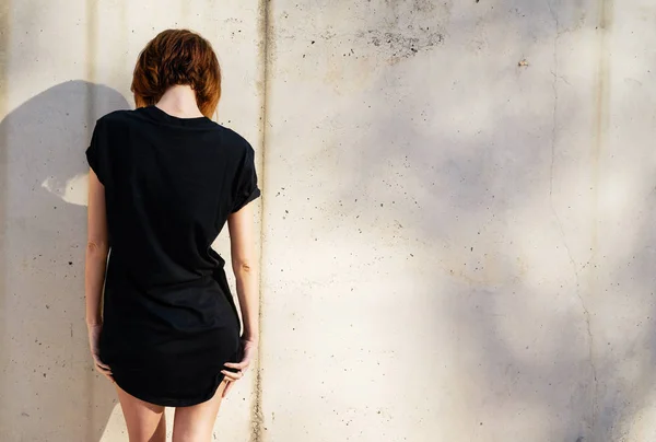 穿着黑色空白 T恤衫的漂亮年轻女子摆出一堵混凝土墙的背景 — 图库照片