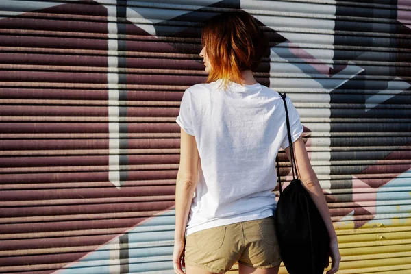 穿着白色空白 T恤衫的年轻女子站在涂鸦墙背景上 后视图 — 图库照片