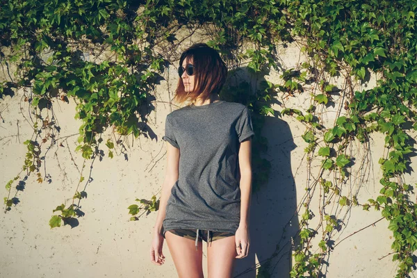 美丽的年轻女子在灰色的空白反对墙壁杂草丛生的常春藤 — 图库照片