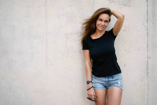 シャツ ポーズ灰色のコンクリートの壁の背景に身に着けている美しい若い女性 — ストック写真