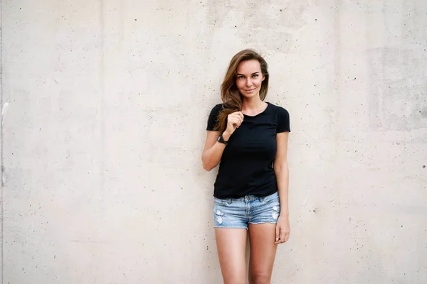 美丽的年轻女子穿着黑色的 T恤衫摆在灰色的混凝土墙背景 — 图库照片