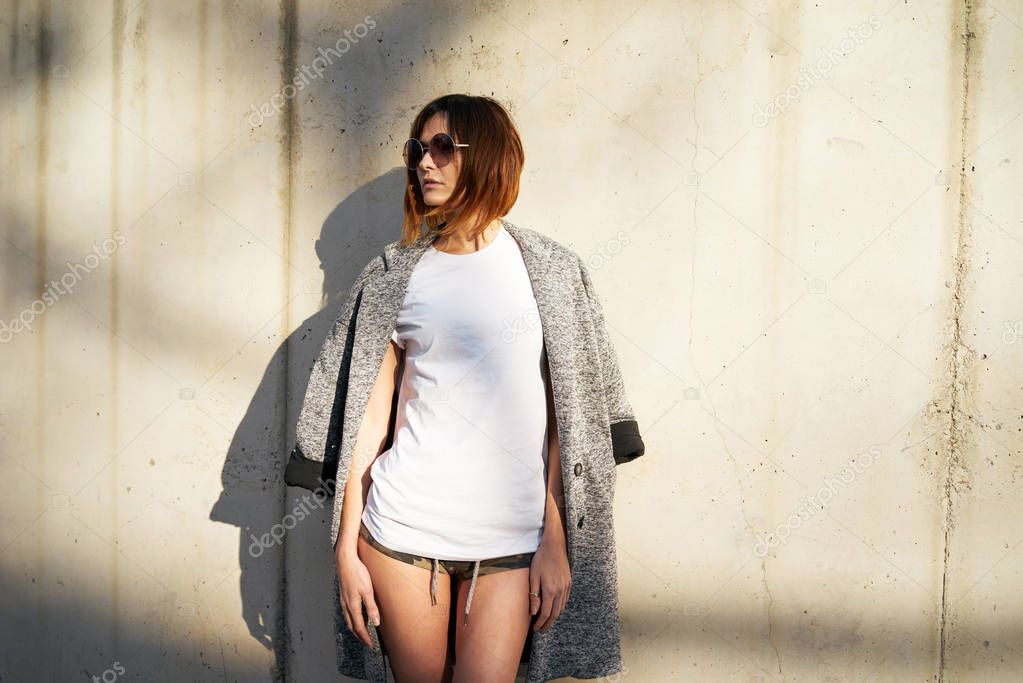 Attractive young woman wearing white blank t-shirt and sunglasses posing against a background of a concrete wall