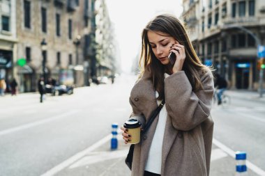 Smartphone ile belgili tanımlık yol onun elinde boş kağıt bardak ile geçerken konuşmaya uzun saçlı güzel kadın 