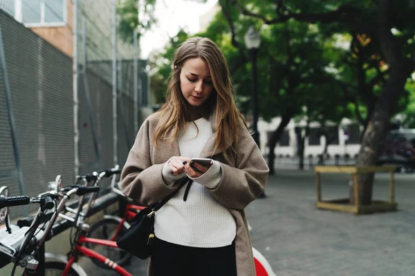 Professional blogger renting bike by smartphone application to avoid traffic jam on the way. Hipster girl making payment transaction online by a mobile phone to pay for the bicycle rent