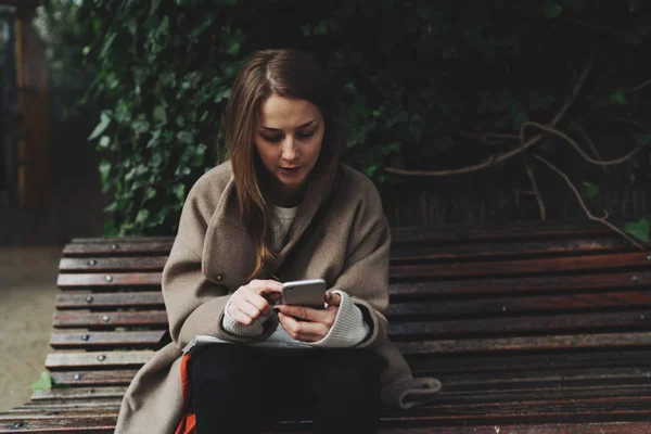 Jovem Mulher Uma Roupa Moda Usando Smartphone Enquanto Sentado Banco — Fotografia de Stock