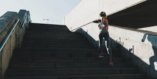 Female athlete running up the stairs with the speed. Sporty young woman in light gray training suit working out outdoors while jogging up the steps. Slim female runner in a good sport shape running.