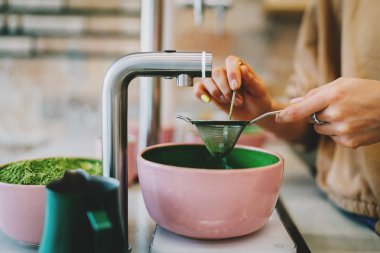 Geleneksel çay seremonisi modern teaware setiyle yapılırken kibrit tozu süzme işlemi. Bir Asya kahve dükkanında matcha çayı hazırlarken bir kadının elleri süzgeç ve kaşıkla çalışıyor..