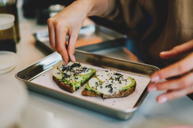 Şef kahvaltıda lezzetli vejetaryen sandviçlere kabak çekirdeği ekliyor. Sağlıklı ve lezzetli glütensiz yemek. Doğal malzemelerle yemek pişirmek. Avokado ve çavdar ekmeği kullanarak basit yemek pişirmek.