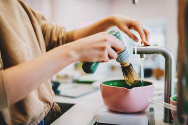 Geleneksel Japon matcha çayı yapma süreci. Barista, matcha çayı için bir kaseye su ekliyor. Kahve dükkanında kibrit tozu çırpmak için modern elektrikli çırpıcı tutan bir kadın eli..