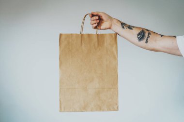 Dövmeli bir elde logo ya da tasarım için boş alan içeren el işi kağıt paketleri, saplı alışveriş çantasının maketi. Beyaz duvar arkaplanı 
