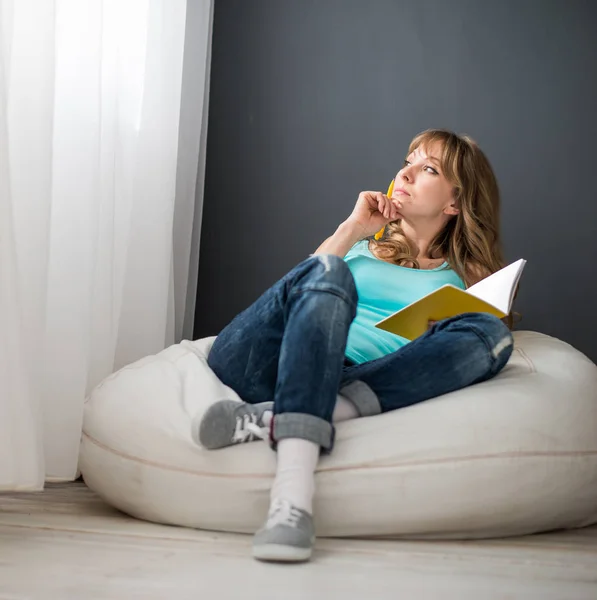 Mujer en la habitación en una silla con un bloc de notas —  Fotos de Stock