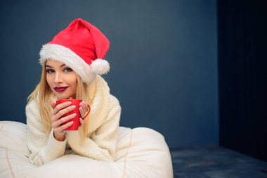 Bir fincan kahve ya da çay tutan Noel Baba şapkası giyen güzel bir kadın portresi