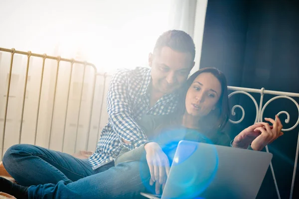 couple sitting in a room on the bed with laptop