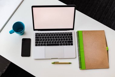 defter, dizüstü bilgisayar ve telefon masanın üstünde.