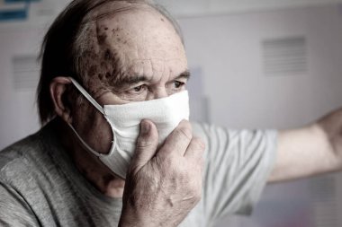 Evde maskeli yaşlı bir adam var.