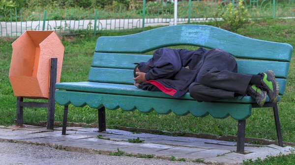 Не трезвый бездомный, спящий на улице на скамейке
