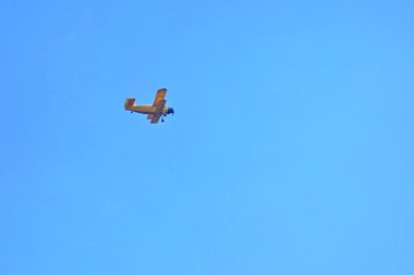 Mavi gökyüzünde sarı bir çift kanatlı uçak uçuyor..