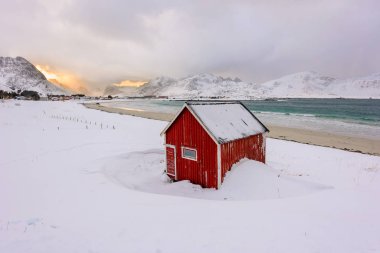 Norveç 'teki Lofoten Adaları ve gün batımındaki güzel kış manzaraları. Karla kaplı plajda kırmızı evi olan Idyllic manzarası. Kuzey Kutup Dairesi 'nde turistik cazibe.