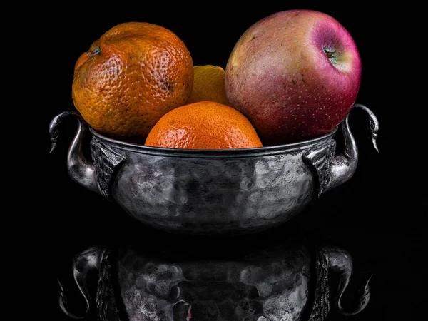 Old fruit bowl with some fruits. Dark background.