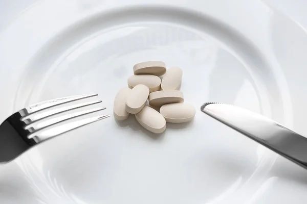 Beyaz hap çatal ve bıçak beyaz tabakta. Yemek yerine hap. Diyet.