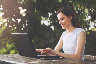 Bir dizüstü bilgisayar kullanarak parkta oturan güzel genç kadın