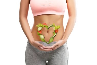 Fit, young woman holding heart  made out of vegetables over her abdomen clipart
