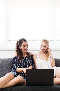 Bir dizüstü bilgisayar kullanarak ve gülümseyen iki genç kadın