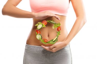 Fit, young woman holding a circle made out of vegetables over her abdomen clipart