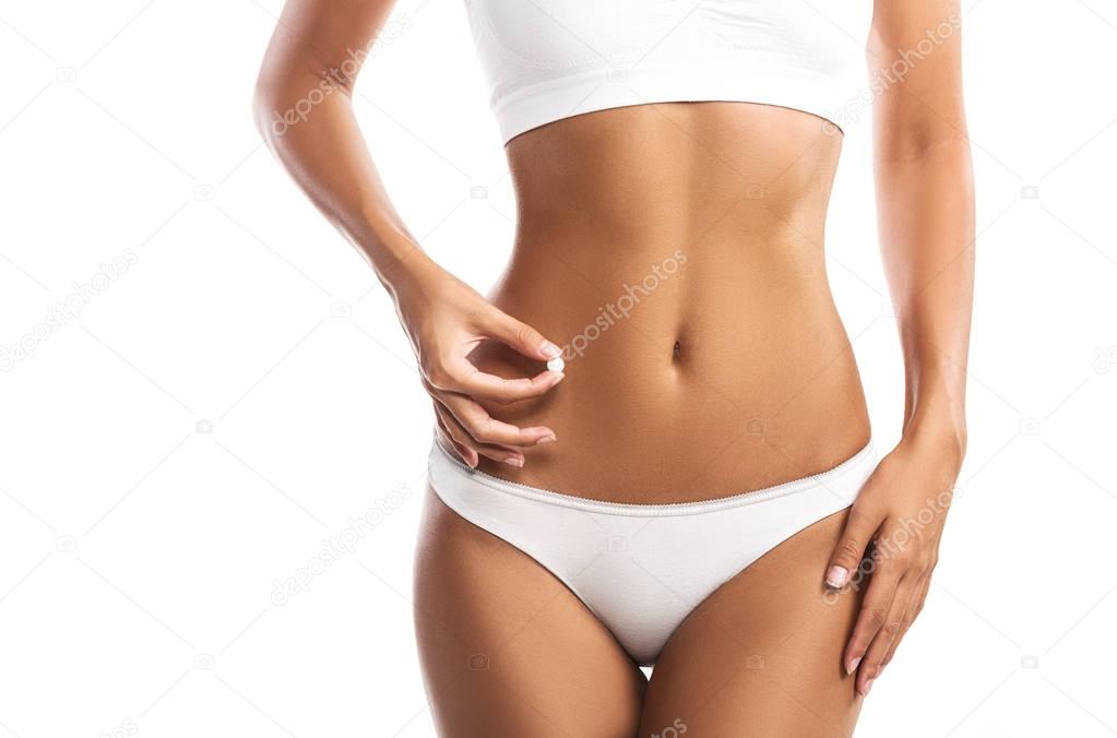 Young woman holding a pill next to her abdomen, isolated on white background, close up