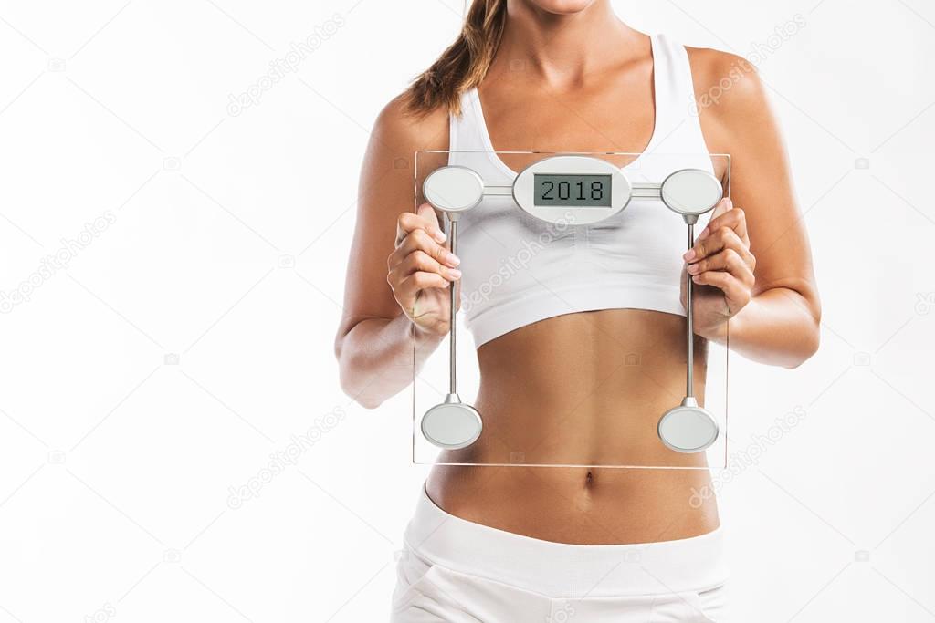 Close up of woman's abdomen, woman holding a weight scale with a year 2018 written on it - New Years weigh t loss resolution
