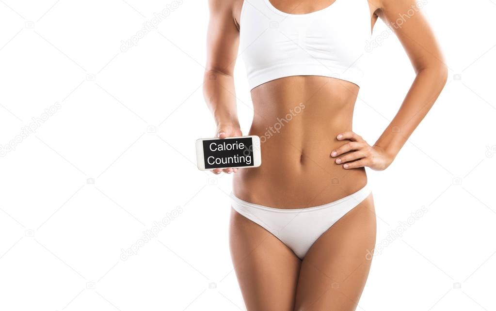 Fit young woman holding a smartphone over her abdomen, isolated on white background