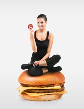 Güzel bir elma tutan bir hamburger üzerinde oturan kız uygun