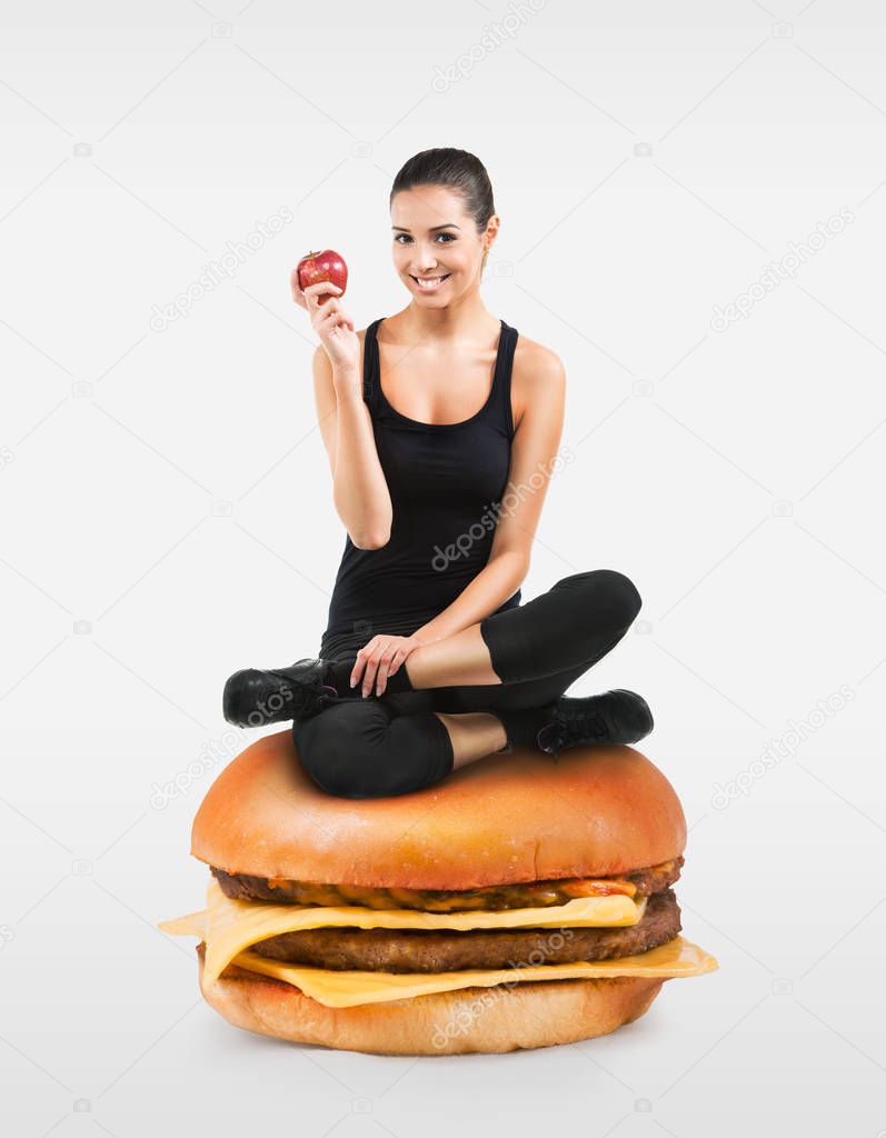 Beautiful fit girl sitting on a hamburger holding an apple
