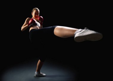 Fit, young, energetic woman kickboxing, black background clipart