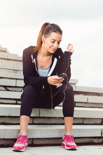 年轻妇女休息从锻炼在外面与手机 — 图库照片