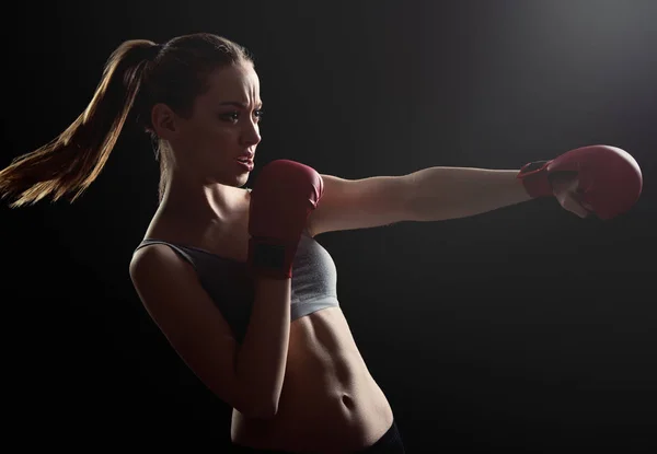 Fit, young, energetic woman boxing, black background