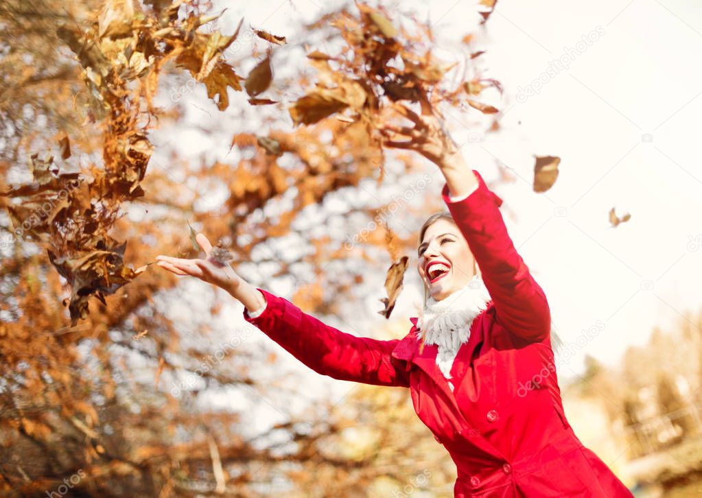 Happy, young woman throwing autumn leaves