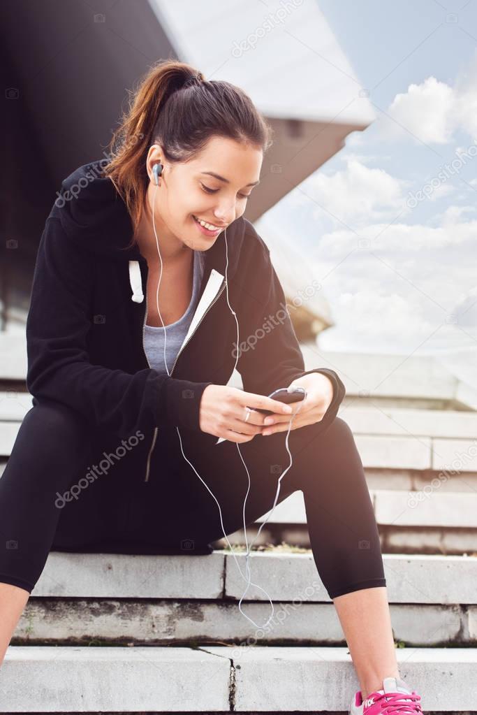 Young woman taking a break from exercising outside with cellphone
