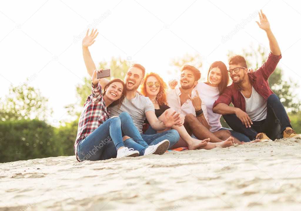 Young men and women having fun outdoors on the beach taking selfie